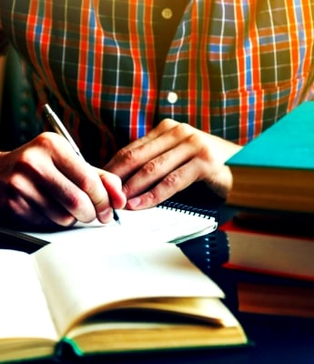 man writing in notebook with a stack of books 832x556 min